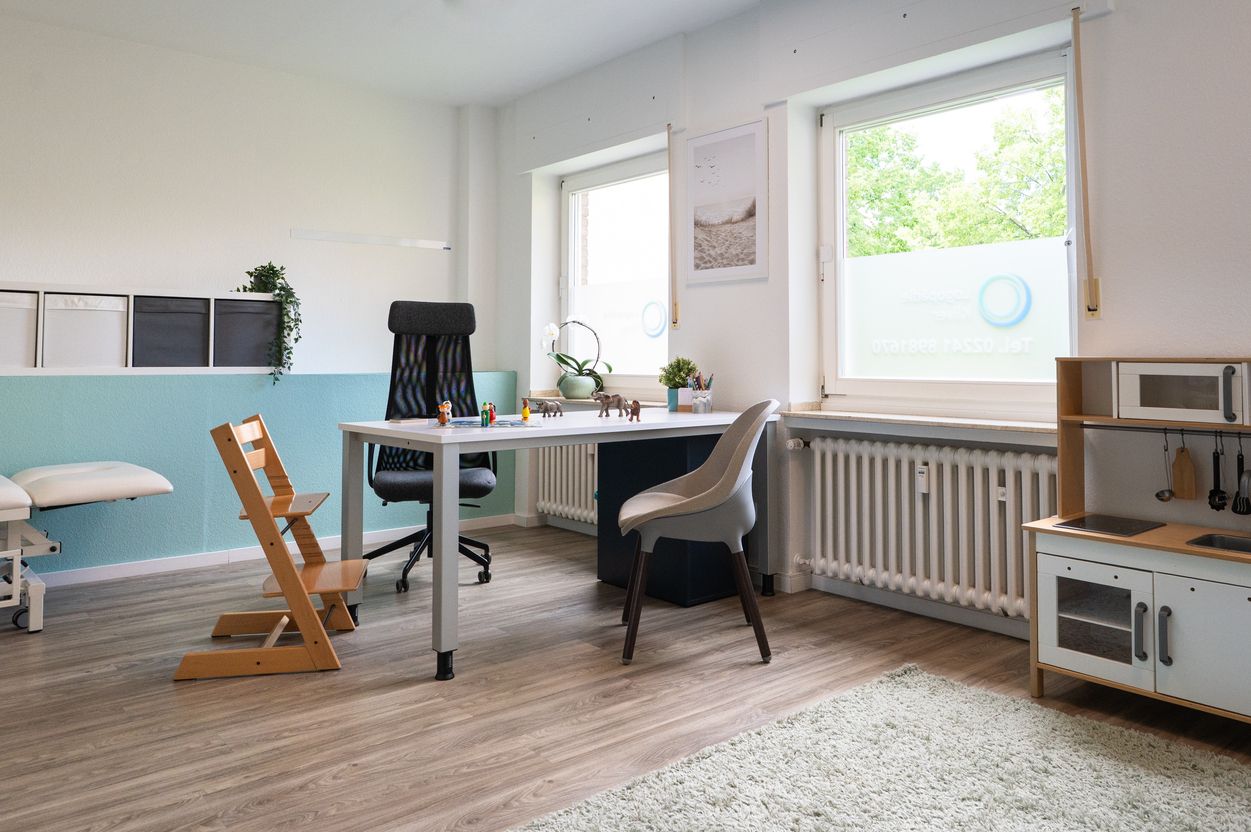 Helles Büro mit Schreibtisch, zwei Stühlen, Fenster mit Rollos und Kinderspielküche